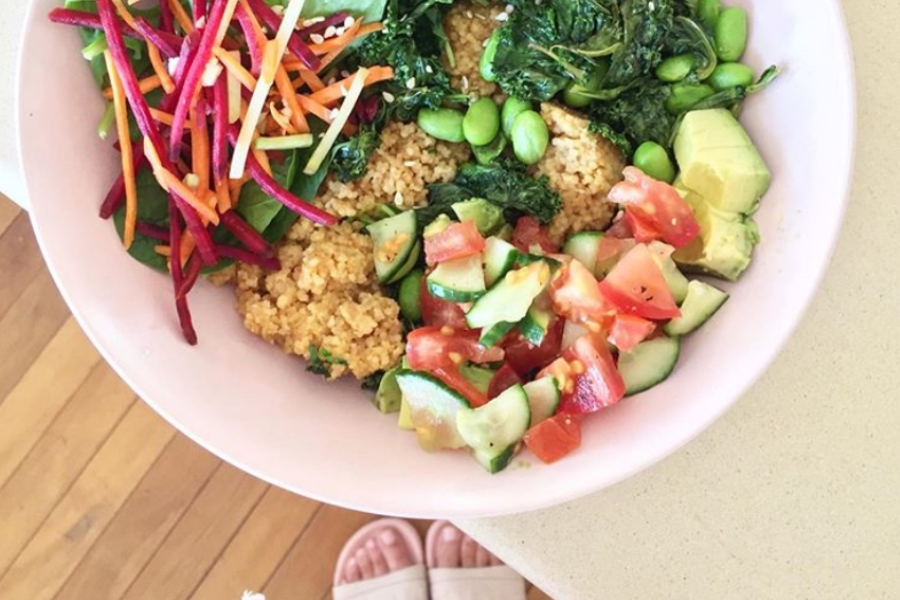 pink bowl of couscous with tomato, cucumber salad and edamame.